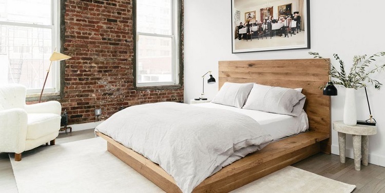 Quarto com cama de madeira em destaque e paredes de tijolo em estilo minimalista.