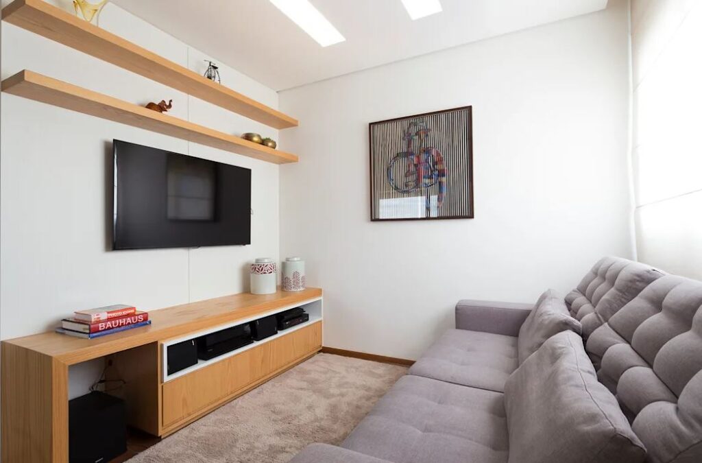 Sala de Tv minimalista com rack e prateleiras em madeira.