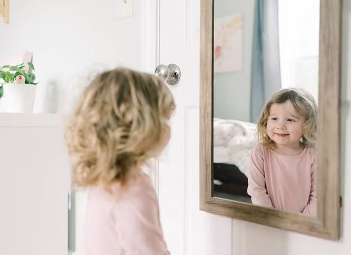Menina se olhando no espelho de seu quarto.