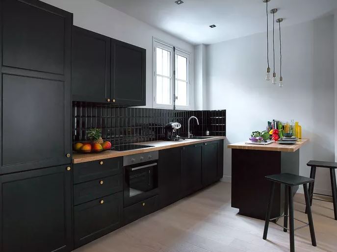 Cozinha com paredes cinzas, armários pretos e assoalho e bancada em madeira amarelada.