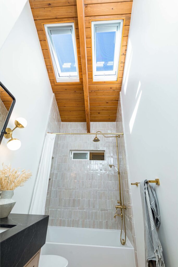 Banheiro com duas claraboias e teto de madeira.
